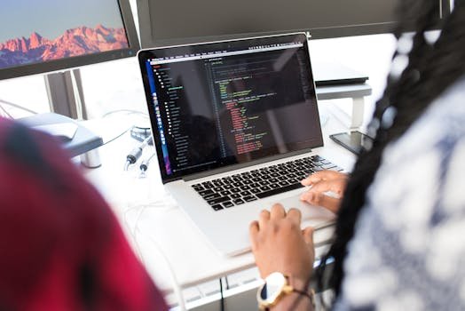 A woman coding on a laptop in a modern office environment with multiple monitors.