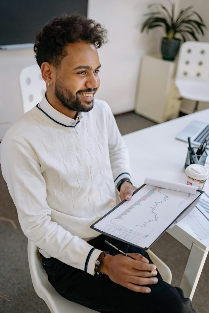 Confident businessman reviews financial data on clipboard, smiling in modern office setting.