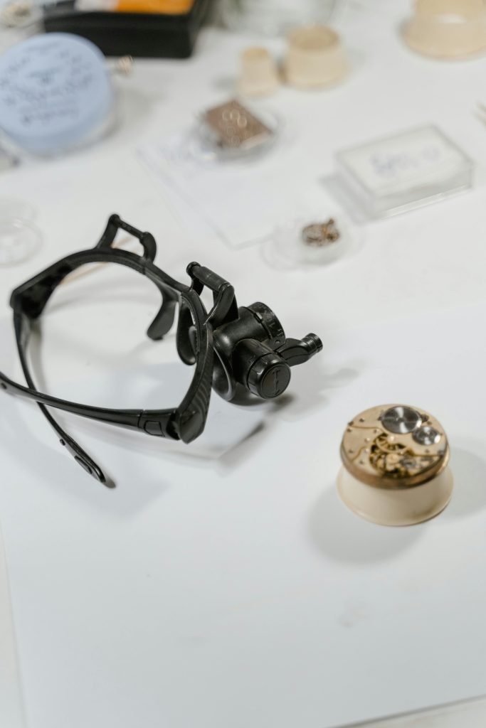 Close-up of watchmaking tools including magnifying glasses and mechanism parts on a desk.